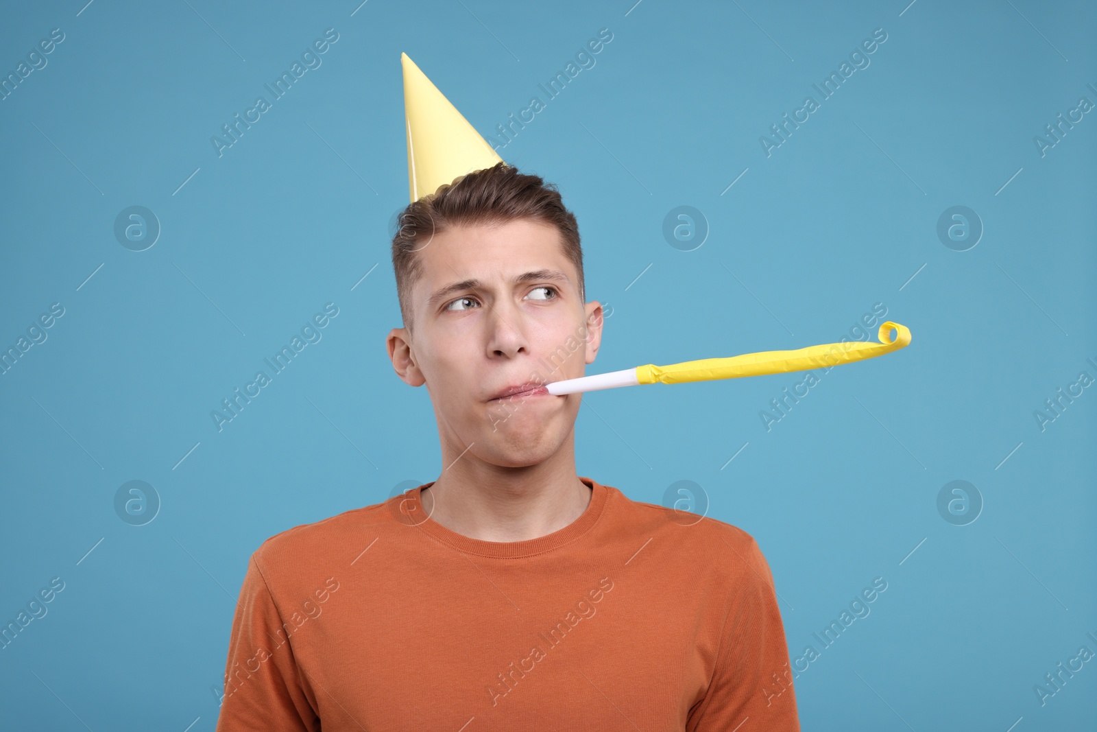 Photo of Young man in party hat with blower on light blue background