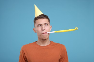 Young man in party hat with blower on light blue background