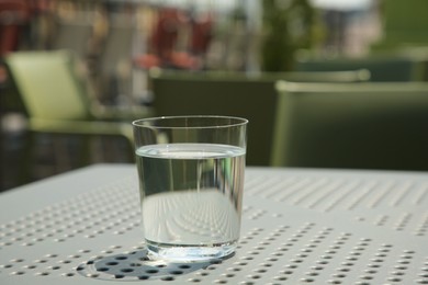Photo of Glass of fresh water on white table outdoors. Space for text
