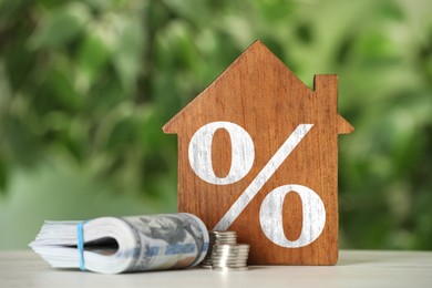 Image of Mortgage rate. Wooden house model with percent sign and money on white table