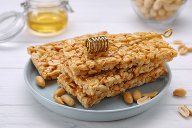 Photo of Delicious peanut bars (kozinaki) and dipper with honey on white wooden table