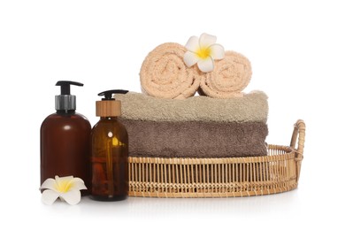 Soft towels in wicker basket, bottles of cosmetic products and plumeria flowers on white background