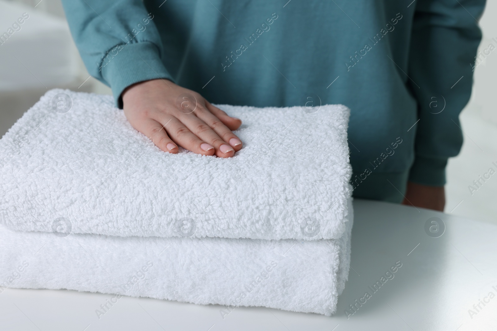 Photo of Woman touching soft white towel indoors, closeup