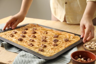 Photo of Woman with baking pan of delicious baklava at wooden table, closeup