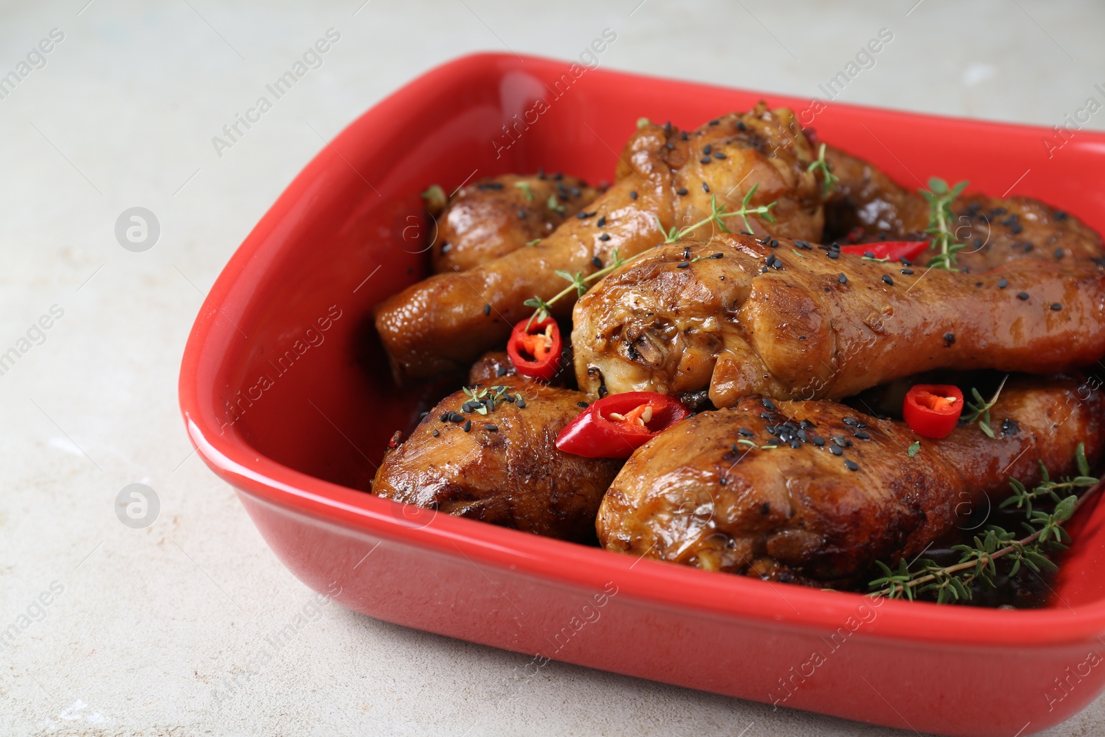 Photo of Chicken legs glazed in soy sauce with black sesame, chili pepper and thyme on light table, closeup