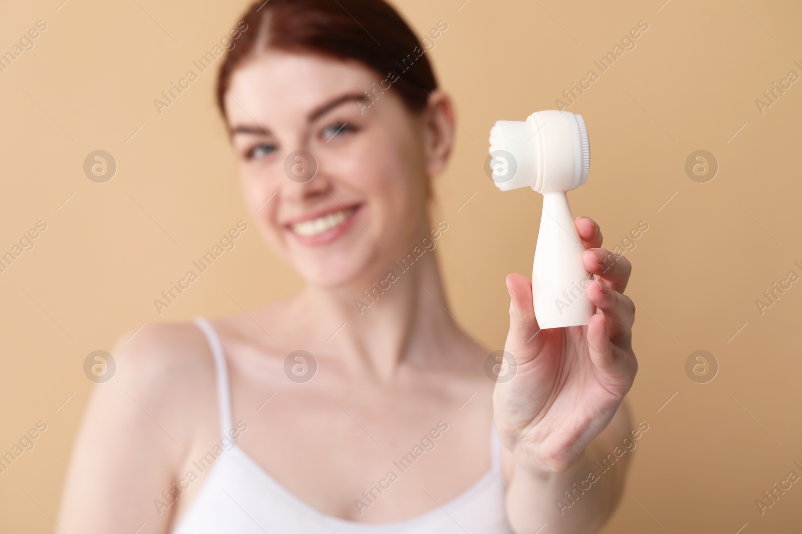 Photo of Washing face. Young woman with cleansing brush on beige background, selective focus