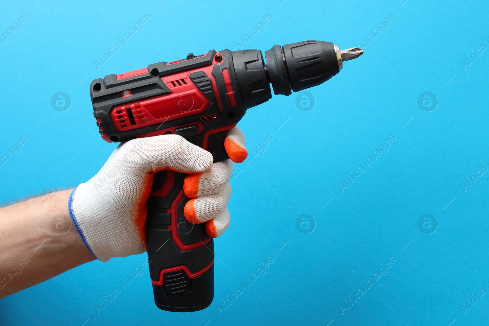 Photo of Handyman holding electric screwdriver on light blue background, closeup. Space for text