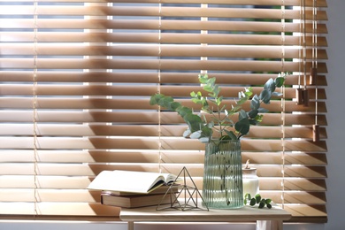 Vase with fresh eucalyptus branches on table near window in room. Interior design