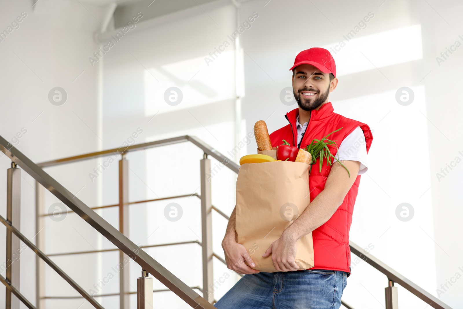 Photo of Man holding paper bag with fresh products on staircase, space for text. Food delivery service