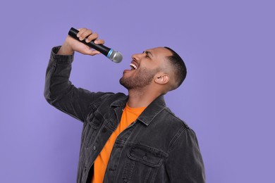 Handsome man with microphone singing on violet background