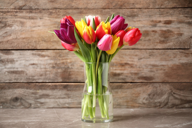 Photo of Beautiful spring tulips in vase on table against wooden background