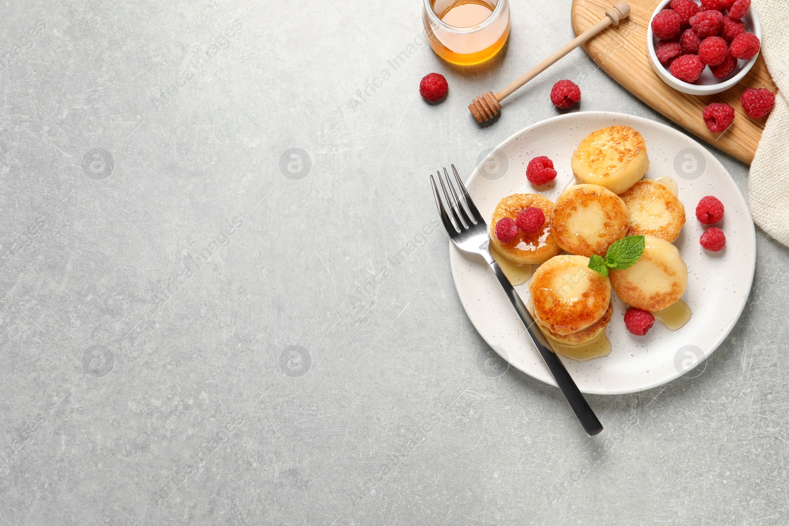 Photo of Delicious cottage cheese pancakes with raspberries and honey on light grey table, flat lay. Space for text