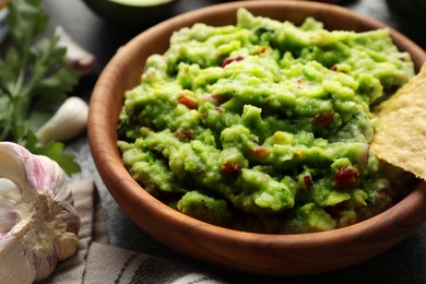 Delicious guacamole with nachos chips and ingredients on table, closeup