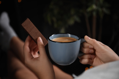 Photo of Woman with wafer and coffee on dark background, closeup. Early breakfast