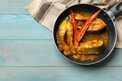 Photo of Tasty fish curry in frying pan on light blue wooden table, top view. Space for text. Indian cuisine