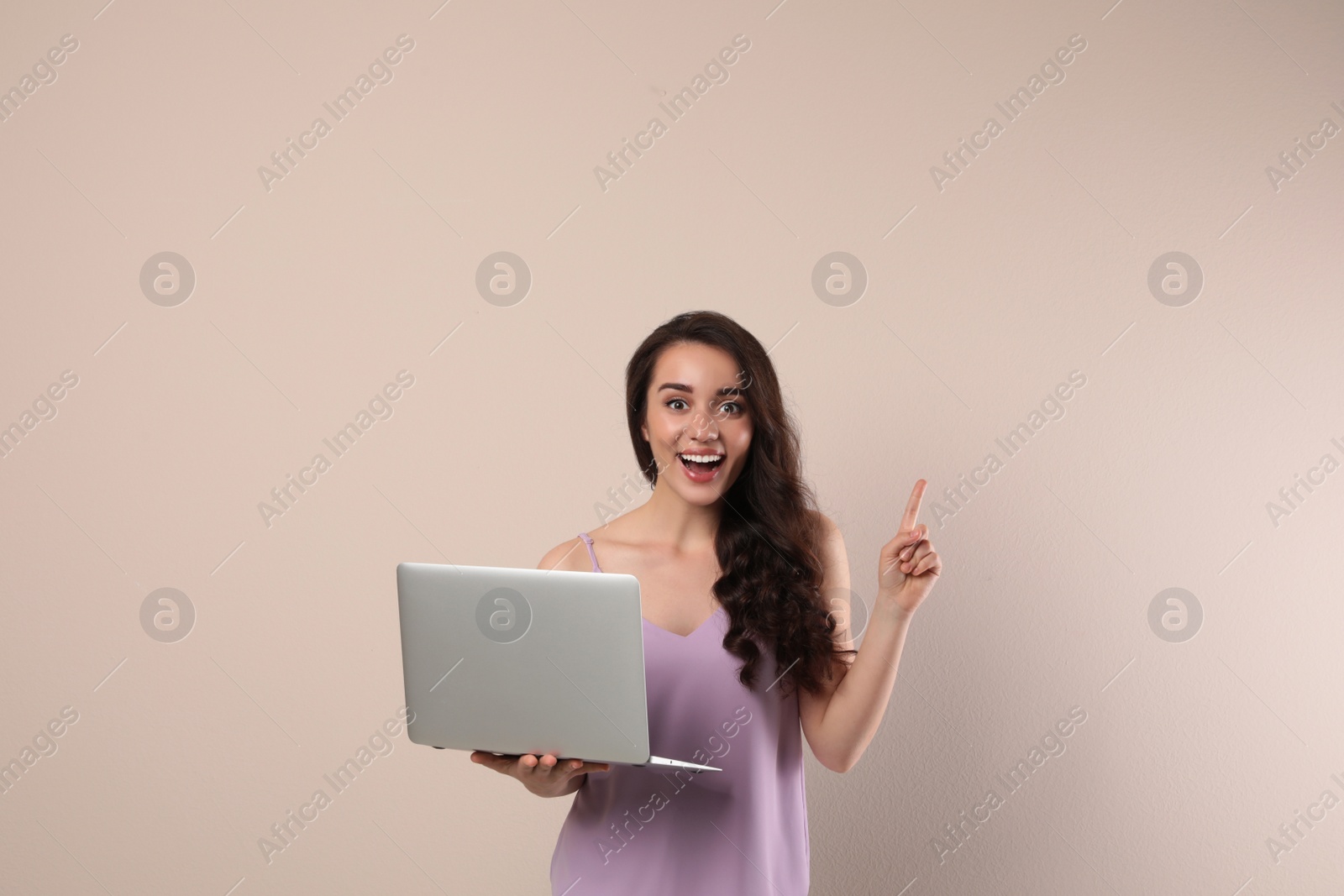 Photo of Excited young woman with laptop on beige background