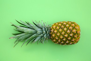 Whole ripe pineapple on light green background, top view