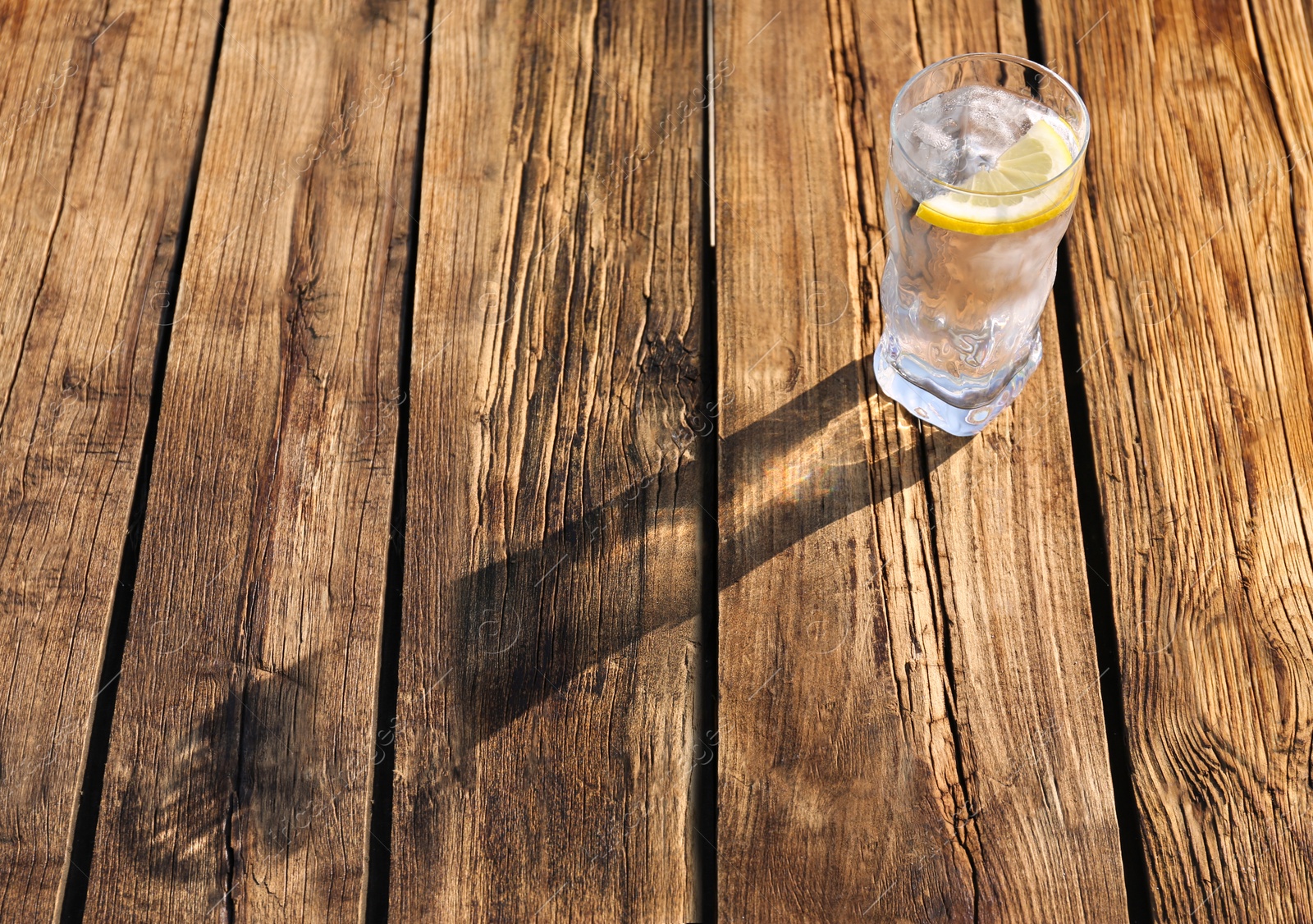 Photo of Glass of refreshing drink with ice and lemon for hot summer day on wooden table, space for text