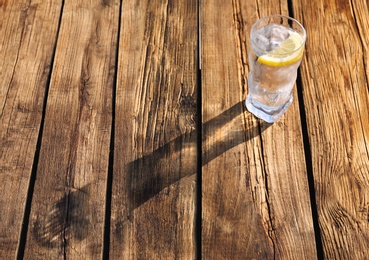 Photo of Glass of refreshing drink with ice and lemon for hot summer day on wooden table, space for text