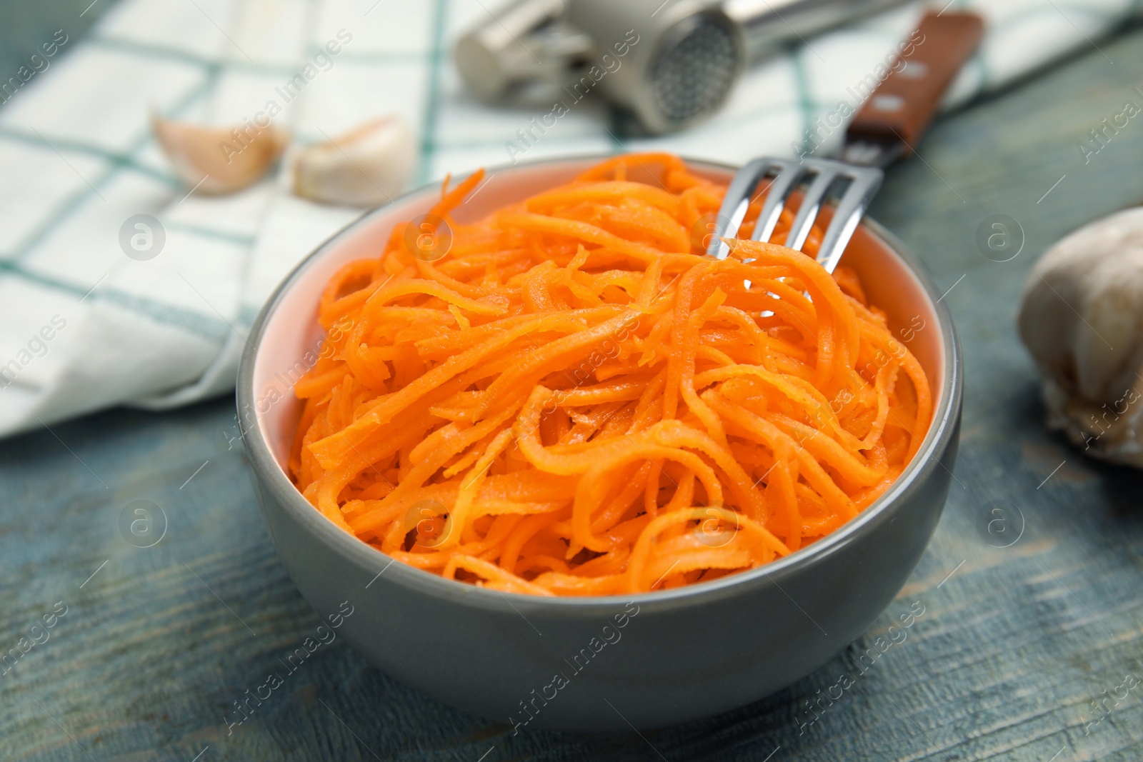 Photo of Delicious Korean carrot salad in bowl on blue wooden table