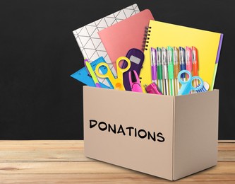 Image of Donation box with different school stationery on wooden table near blackboard