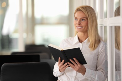 Smiling woman with book in office, space for text. Lawyer, businesswoman, accountant or manager