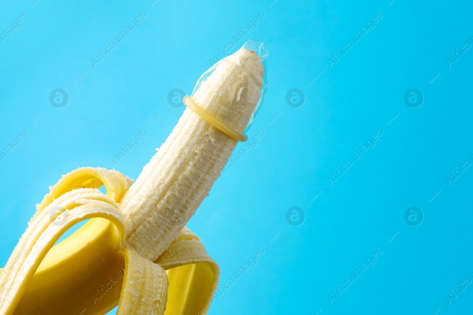 Photo of Banana with condom on light blue background, space for text. Safe sex concept