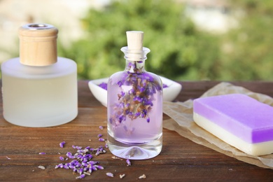 Photo of Natural herbal oil and lavender flowers on table against blurred background