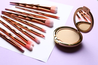 Professional makeup brushes and face powder on color background