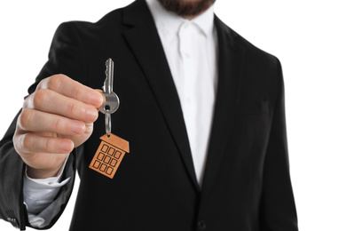 Photo of Real estate agent holding house key with trinket on white background, closeup