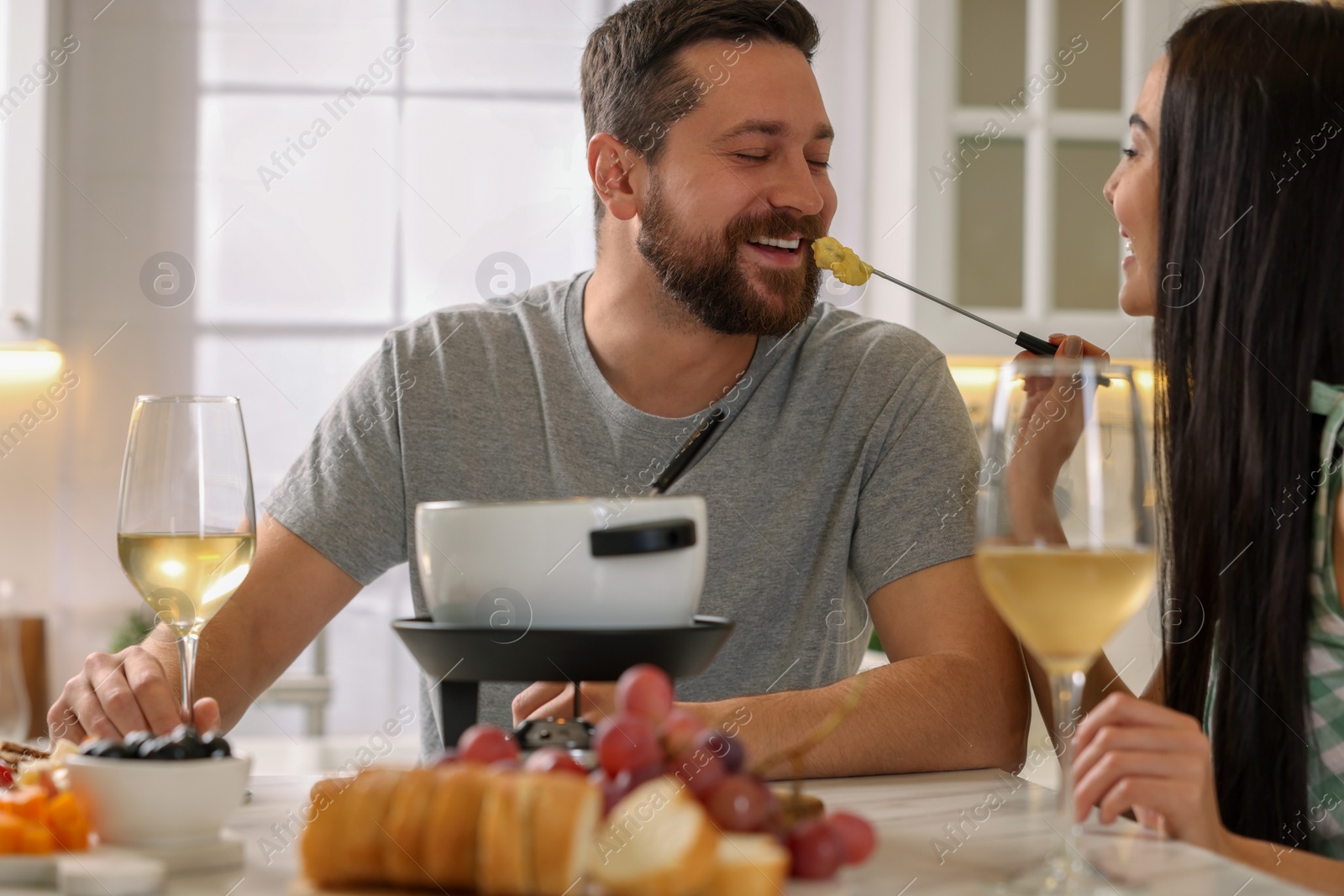 Photo of Affectionate couple enjoying cheese fondue during romantic date in kitchen