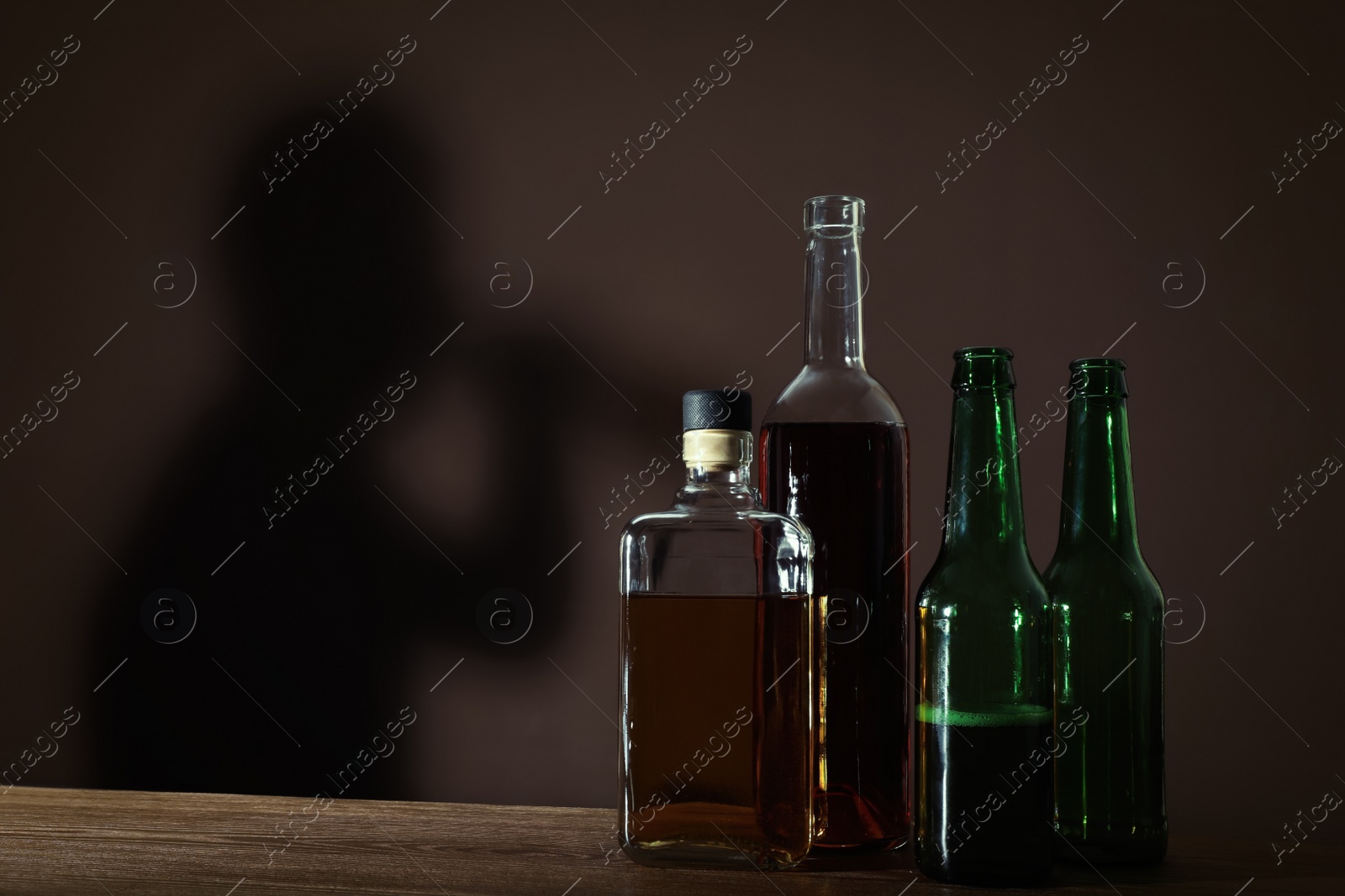Photo of Alcoholic drinks on wooden table against brown wall with shadow of addicted man