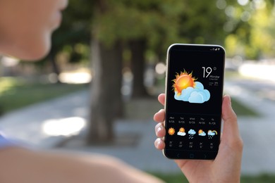 Woman checking weather using app on smartphone outdoors, closeup. Data, sun with cloud and other illustrations on screen