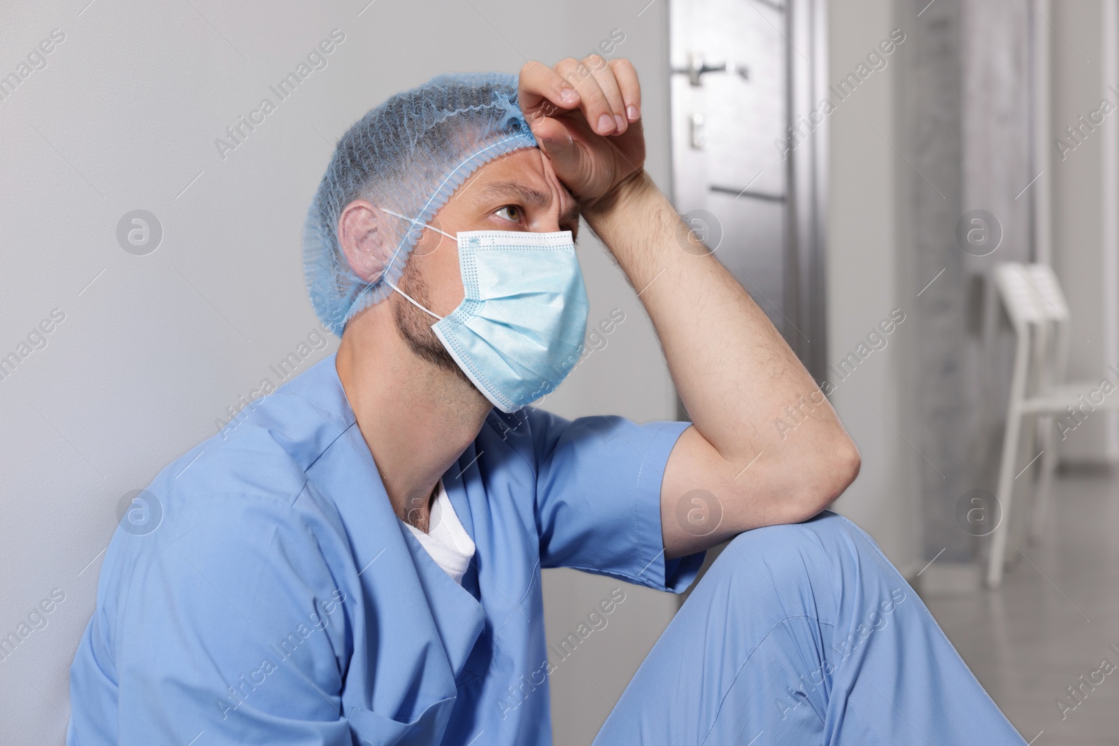 Photo of Exhausted doctor near grey wall in hospital corridor