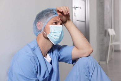 Photo of Exhausted doctor near grey wall in hospital corridor