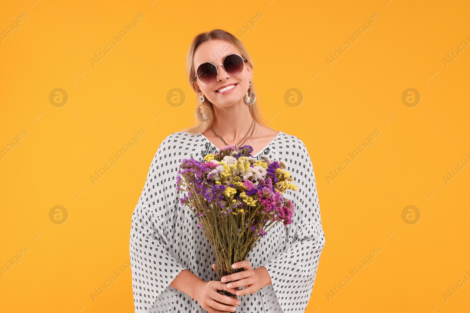 Photo of Portrait of smiling hippie woman with bouquet of flowers on yellow background