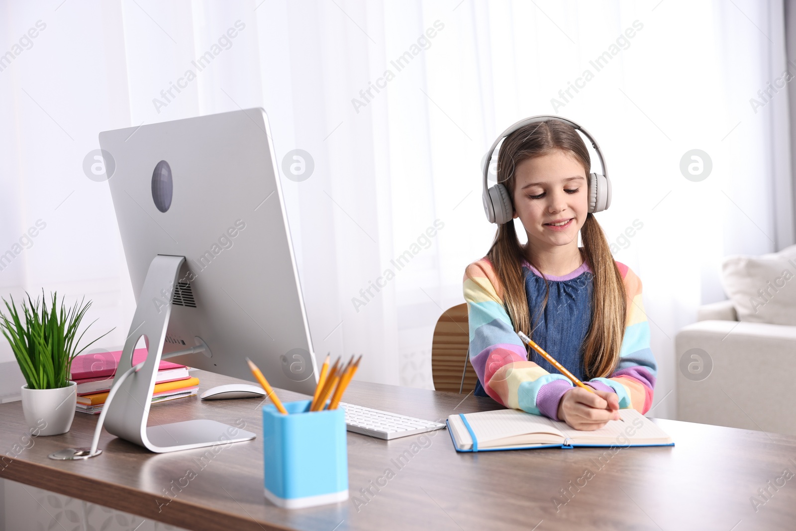 Photo of E-learning. Cute girl taking notes during online lesson at table indoors