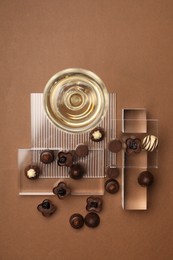 Delicious heart shaped chocolate candies and glass of champagne on brown background, top view