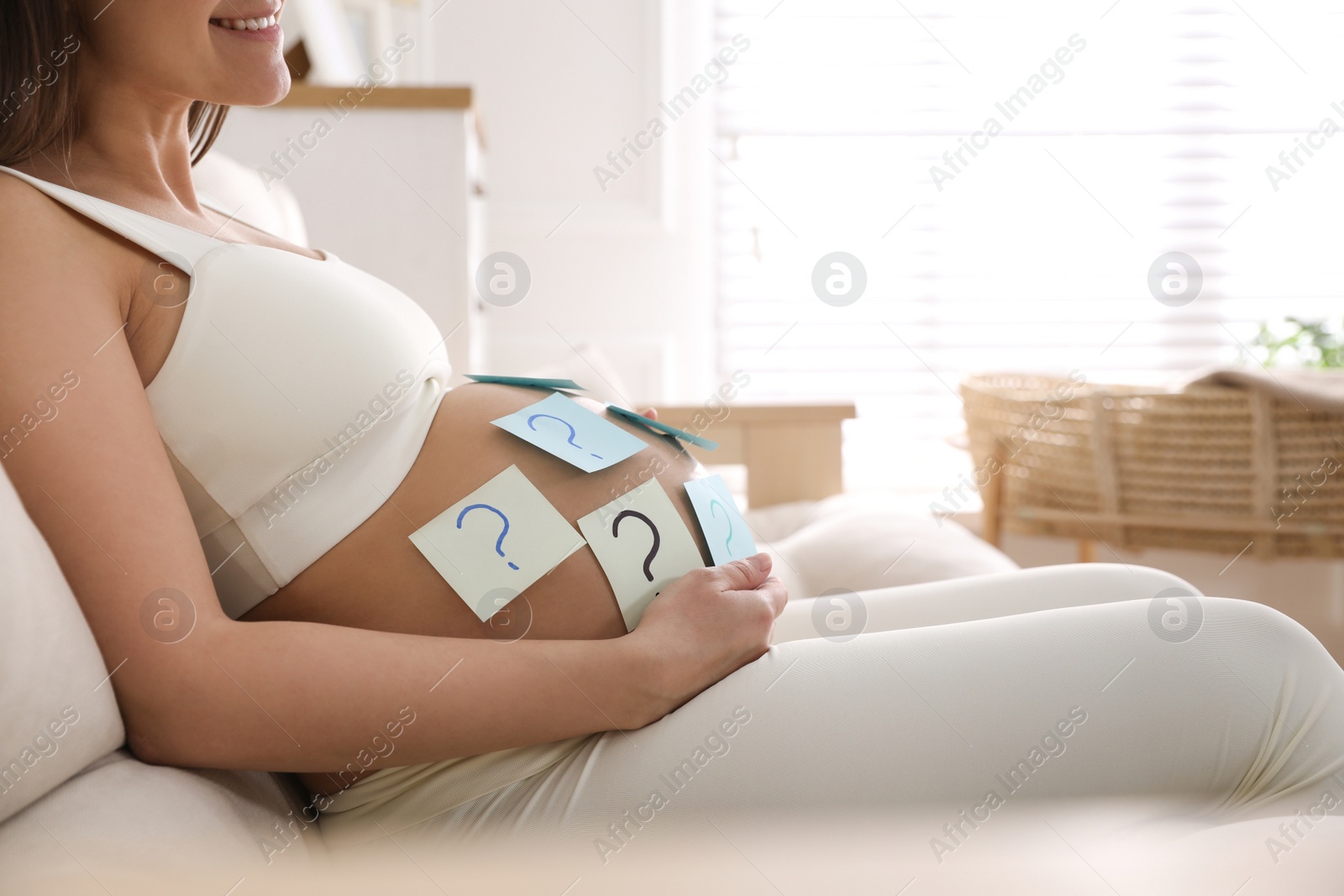 Photo of Pregnant woman with sticky notes on belly indoors, closeup. Choosing baby name