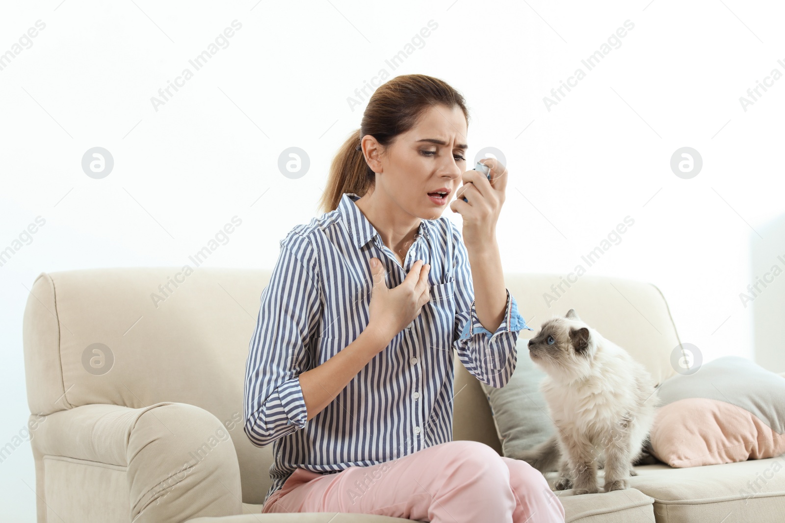 Photo of Woman using asthma inhaler near cat at home. Health care