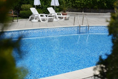 Outdoor swimming pool with handrails and empty sunbeds at resort on sunny day