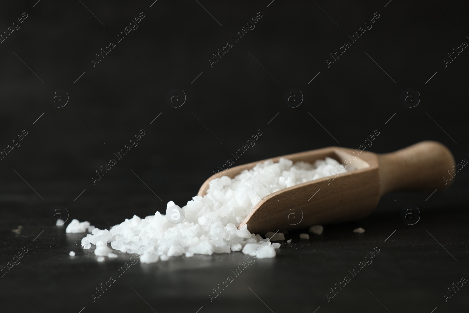 Photo of Organic salt and wooden scoop on black table, closeup. Space for text