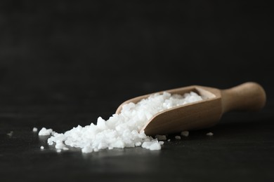 Photo of Organic salt and wooden scoop on black table, closeup. Space for text