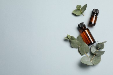 Aromatherapy. Bottles of essential oil and eucalyptus leaves on light grey background, flat lay. Space for text