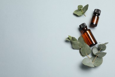 Photo of Aromatherapy. Bottles of essential oil and eucalyptus leaves on light grey background, flat lay. Space for text