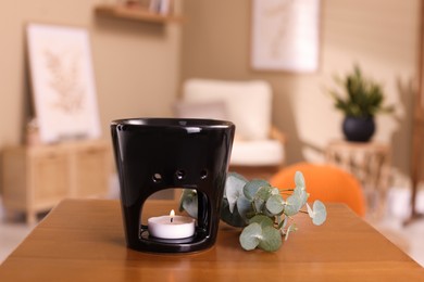 Photo of Stylish aroma lamp with small candle near eucalyptus branch on wooden table indoors