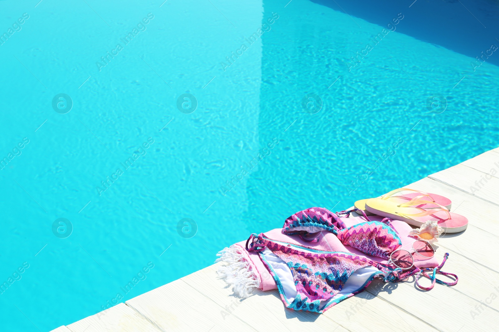 Photo of Beach accessories on wooden deck near swimming pool. Space for text