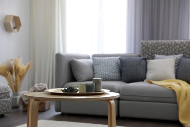 Photo of Wooden table with candles and tray near sofa in living room. Interior design