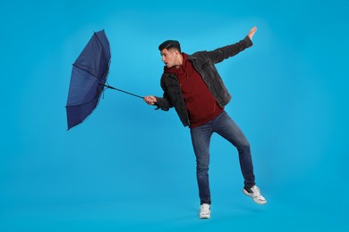 Photo of Man with umbrella caught in gust of wind on light blue background