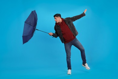 Man with umbrella caught in gust of wind on light blue background